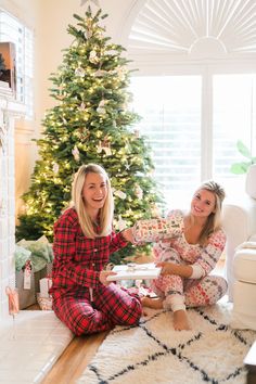 two women sitting on the floor in front of a christmas tree