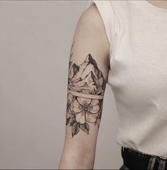 a woman's arm with a flower tattoo on it and mountains in the background