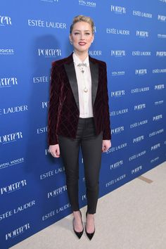 a woman standing in front of a blue wall wearing a red velvet jacket and black pants