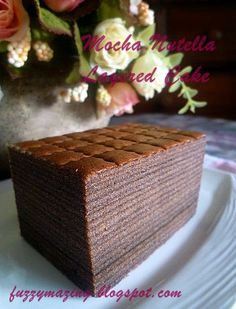 a piece of chocolate cake sitting on top of a white plate next to a vase with flowers