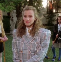 two women are standing in the grass and one is wearing a plaid jacket with a bow tie