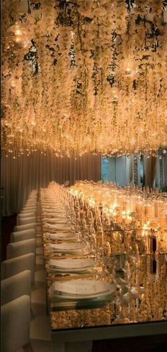 a very long table with many glasses and place settings on it, surrounded by chandeliers