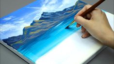 a person is holding a pencil and drawing on a piece of paper with blue mountains in the background