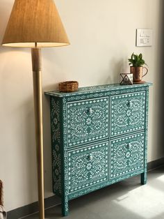 a green and white painted dresser next to a lamp