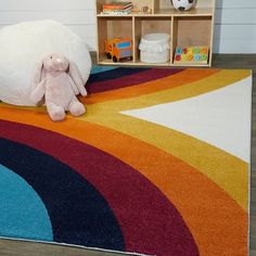 a stuffed animal sitting on top of a rainbow rug in front of a bookshelf