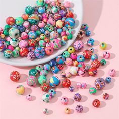 there are many different beads in the bowl next to each other on the table with pink background