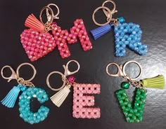 six key chains with letters made out of beads and tassels on black surface