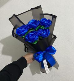 a person holding a bouquet of blue roses in a black paper bag with a blue ribbon