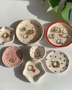 seven pieces of porcelain jewelry sitting on top of a white surface next to a green plant