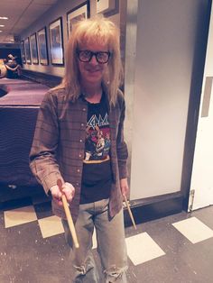 a man with long blonde hair and glasses holding a stick in his hand while standing on a checkered floor