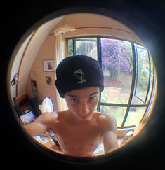 a man with no shirt wearing a hat looking at the camera through a round window