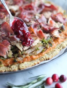 a person spooning cranberry sauce onto a pizza