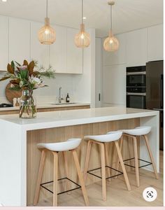 a kitchen with three stools next to an island and two lights hanging from the ceiling