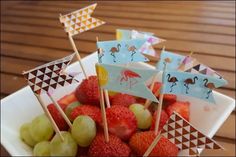 strawberries and grapes are arranged in a bowl on a table, with small flags sticking out of them