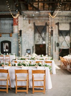 tables with white linens and greenery are set up in an old warehouse for a wedding reception