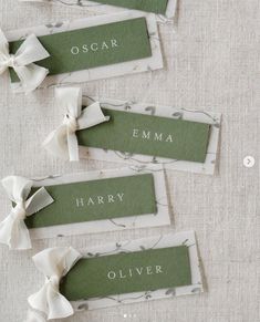 three name tags with bows on them sitting on top of a white tablecloth covered table