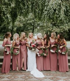 a group of women standing next to each other in front of trees and bushes with bouquets