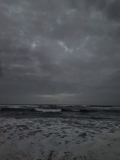 an empty beach with waves coming in to shore and dark clouds above the ocean on a gloomy day