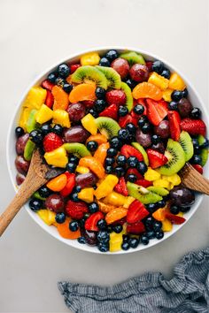 a white bowl filled with fruit and topped with a wooden spoon on top of a table