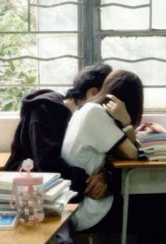 two people hugging each other in front of a desk with books and bottles on it