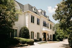 a large white house with lots of windows and bushes around it's front entrance