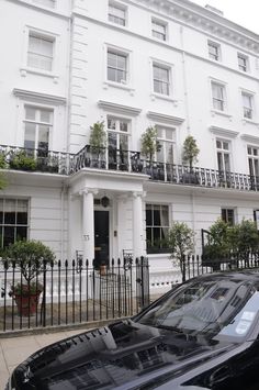 a black car parked in front of a tall white building with balconies on it