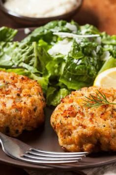 two crab cakes are on a plate with salad and lemon wedges next to it