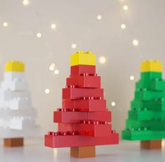 three lego christmas trees are shown in front of a white wall with lights behind them