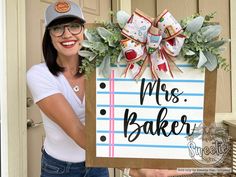 a woman holding up a sign that says mrs bake and wreath on the front door