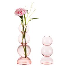 a pink flower sitting in a vase next to three clear glass balls on a white background