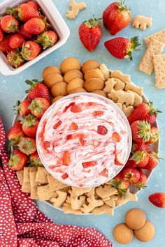 a bowl of fruit dip surrounded by crackers and strawberries on a blue surface