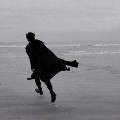 a man is running on the beach with his coat over his head and feet in the air