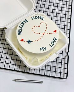 a cake in a container with the words welcome home my love written on it, sitting on a cooling rack