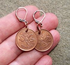 a person is holding two canadian coins in their hand and they are wearing tiny earrings