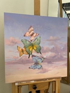 an easel with a painting on it that has three butterflies flying in the sky