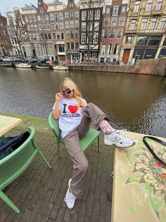 a woman sitting on a green chair next to a body of water with buildings in the background