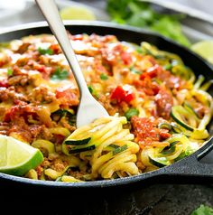 a skillet filled with pasta, meat and veggies next to lime wedges