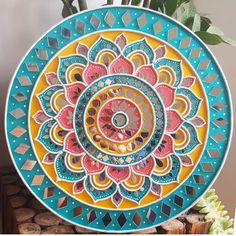 a colorful plate sitting on top of a table next to a potted plant and wooden slices