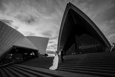 a bride and groom are standing on the stairs in front of the sydney opera house