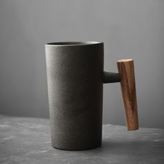 a black cup with a wooden handle sitting on top of a gray table next to a grey wall