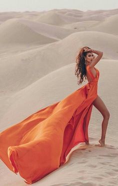 a woman in an orange dress standing on sand dunes