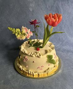 a cake decorated with flowers and leaves on a platter against a blue background,