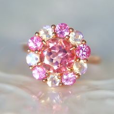 Pink Tourmaline Ring Pink spinel Rainbow Moonstone halo ring Edwardian style halo ring solid yellow gold pink engagement ring One-of-a-kind Pink Tourmaline Ring with Blue Moonstone and Pink Spinel Halo in 14K Rose Gold Add a touch of elegance to your jewelry collection with our custom designer cut natural pink tourmaline ring. The showstopper of this ring is a natural pink tourmaline, cut in a unique designer cut, measuring 6mm x 6mm. The tourmaline is surrounded by a double halo of blue moonstone and pink spinel. The blue moonstone adds a pop of color and contrast to the overall design while the pink spinel adds a touch of feminine charm. The ring is set in a 14K rose gold, which adds a touch of warmth and vintage charm to the overall design. The ring is inspired by the Edwardian era, wit Pink Engagement, Pink Engagement Ring, Spinel Ring, Pink Spinel, Edwardian Style, Pink Tourmaline Ring, Blue Moonstone, Double Halo, Tourmaline Ring