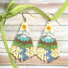 a pair of colorful beaded earrings hanging from a green ribbon on top of a wooden table