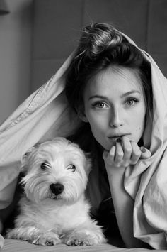 a black and white photo of a woman laying on a bed with a dog under her blanket