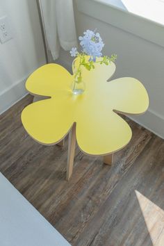 a yellow table with flowers on it in front of a window and wooden flooring