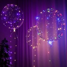 two balloons with lights on them are in front of a purple curtain and christmas tree