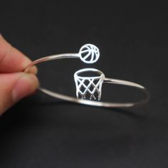 a hand is holding a silver wire bracelet with basketballs on it and a basket in the middle