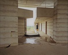 an empty room with concrete walls and flooring in the foreground, looking out onto a field