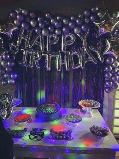 a table topped with lots of purple and silver balloons next to a cake covered in confetti